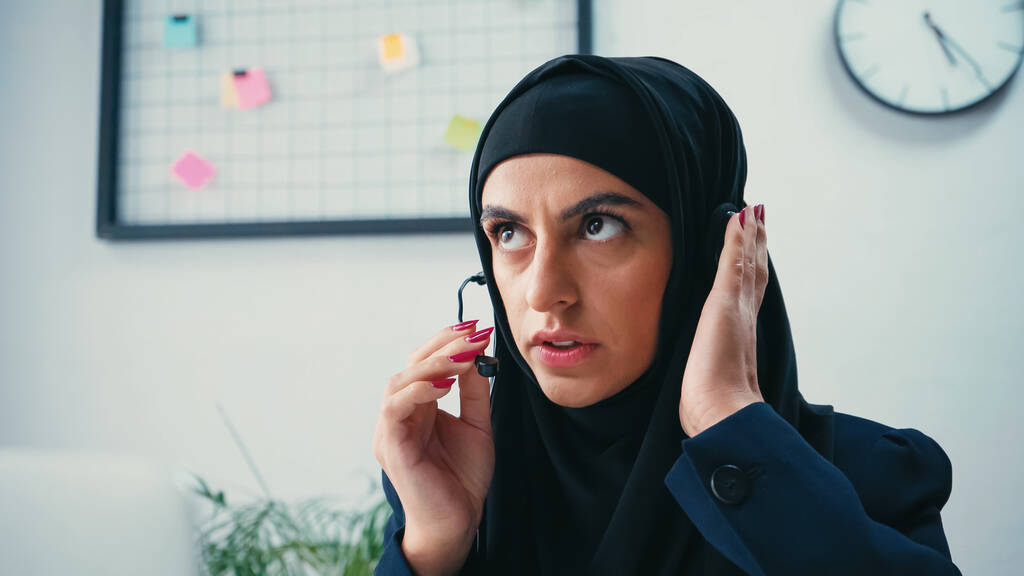 Muslim woman in hijab using headset and looking up in call center  - Photo, Image