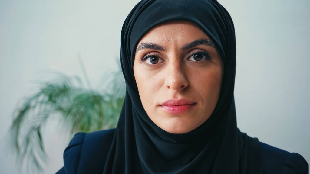 Nahaufnahme einer jungen muslimischen Geschäftsfrau im Hidschab, die im Büro in die Kamera blickt  - Foto, Bild