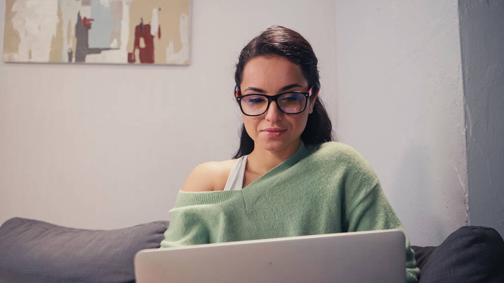 Freelancer en gafas de vista mirando borrosa portátil en casa  - Foto, Imagen