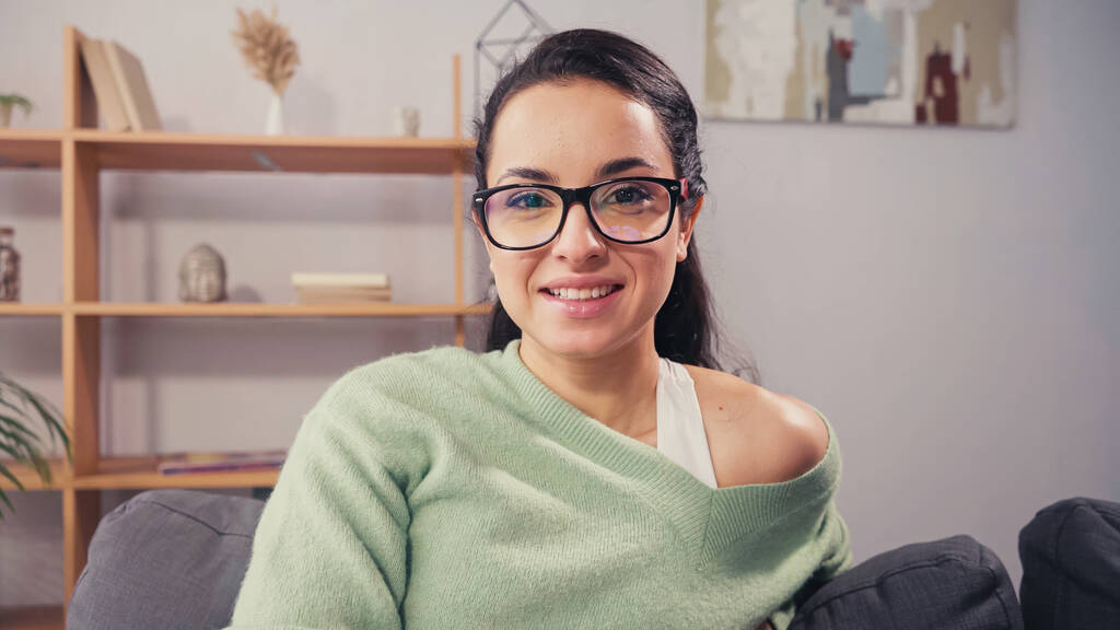 Młoda kobieta w okularach uśmiechnięta do kamery na kanapie  - Zdjęcie, obraz