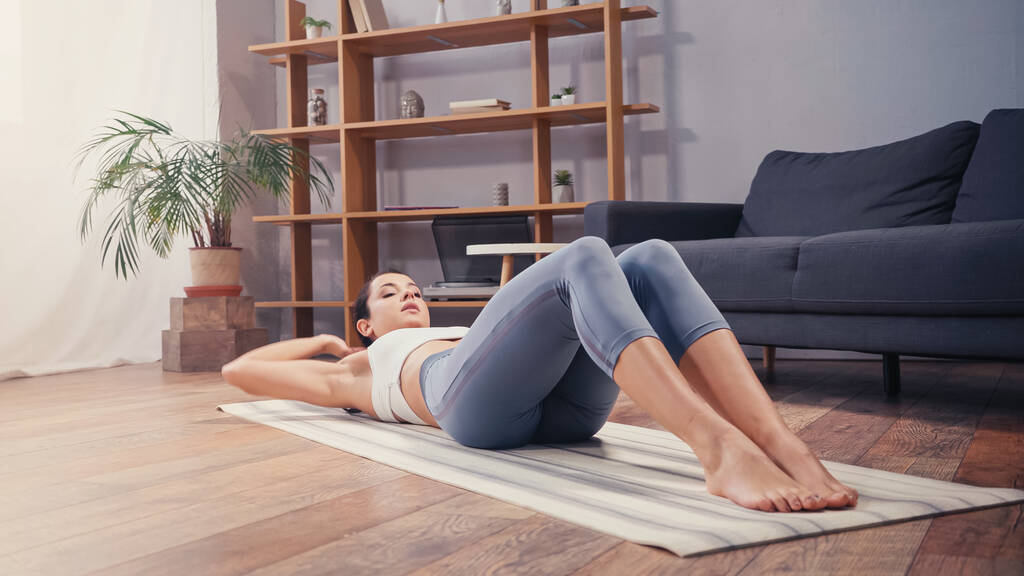 Sportvrouw liggend op fitness mat tijdens de training thuis  - Foto, afbeelding