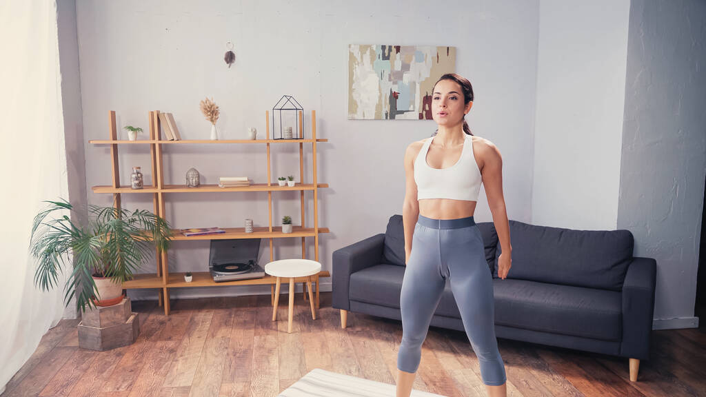 Brunette femme en vêtements de sport debout sur tapis de fitness à la maison  - Photo, image