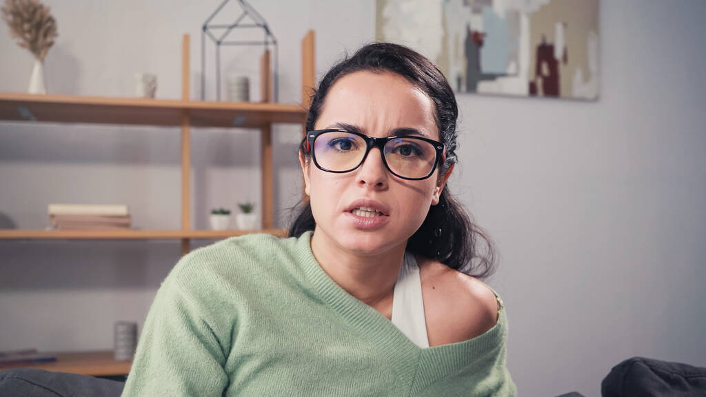 Fokussierte Frau mit Brille blickt zu Hause in die Kamera  - Foto, Bild
