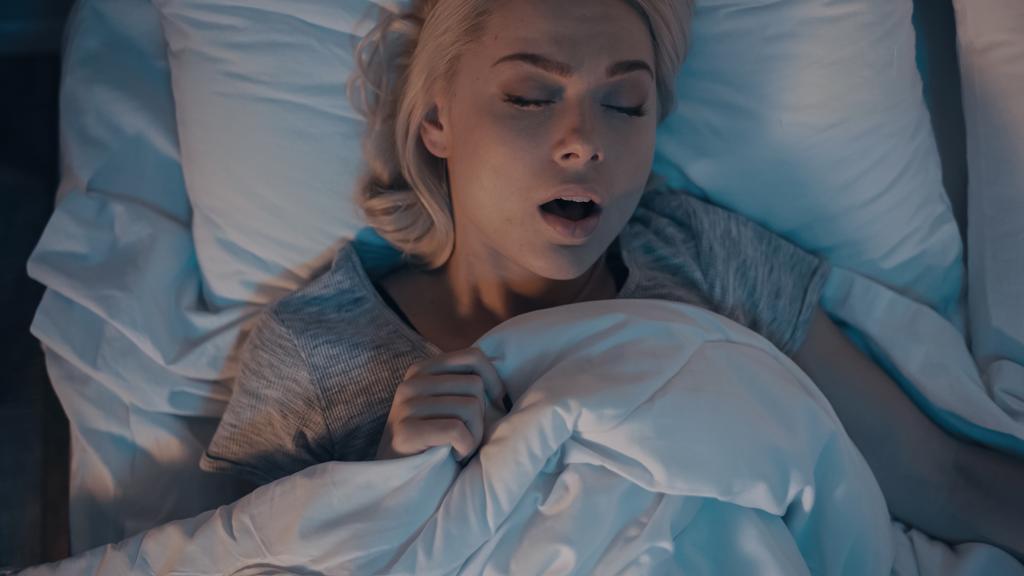 Eine junge Frau schnarcht von oben, während sie im Bett schläft  - Foto, Bild