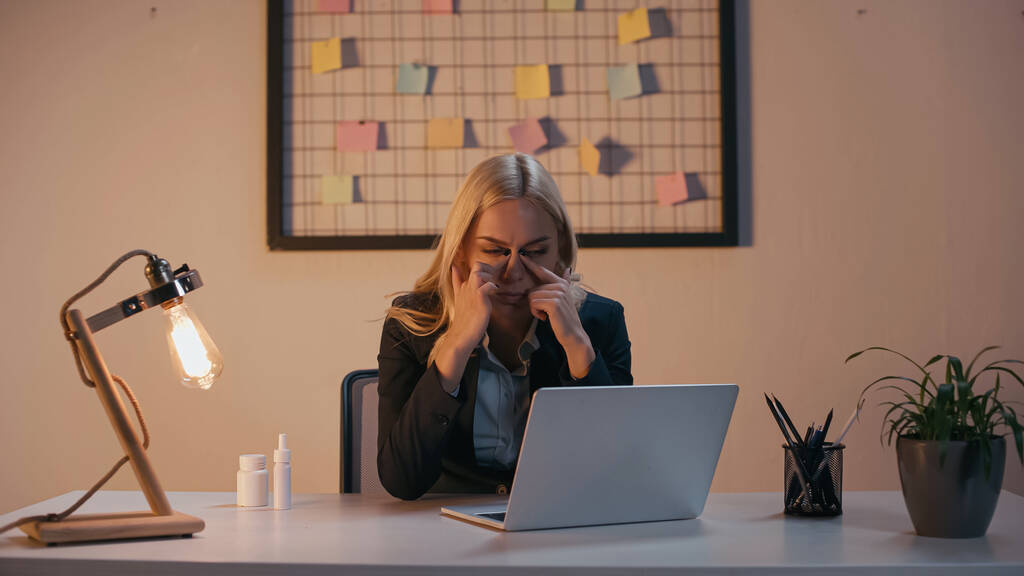 Mujer de negocios que sufre de secreción nasal cerca de la computadora portátil y pastillas en la mesa en la oficina  - Foto, imagen
