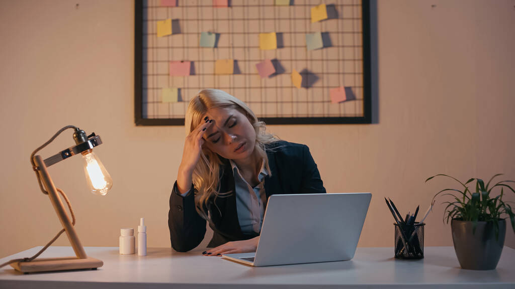 Mujer de negocios cansado sentado cerca de la computadora portátil y pastillas en la oficina  - Foto, imagen