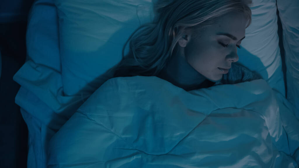 Κάτοψη της γυναίκας που κοιμάται σε λευκό κρεβάτι τη νύχτα  - Φωτογραφία, εικόνα