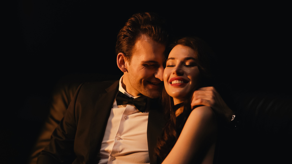 homme en costume étreignant et flirtant avec heureux femme isolé sur noir  - Photo, image
