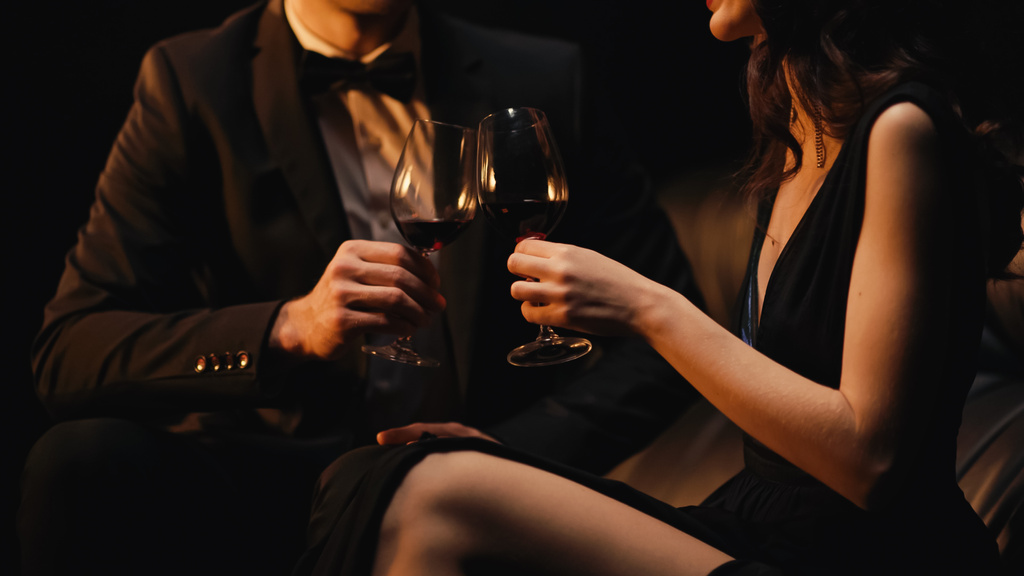 vista ritagliata di coppia bicchieri di vino rosso mentre seduto sul divano isolato su nero - Foto, immagini