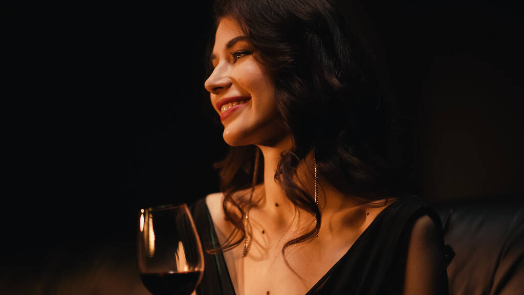 radosna kobieta trzymająca kieliszek wina na czarno - Zdjęcie, obraz