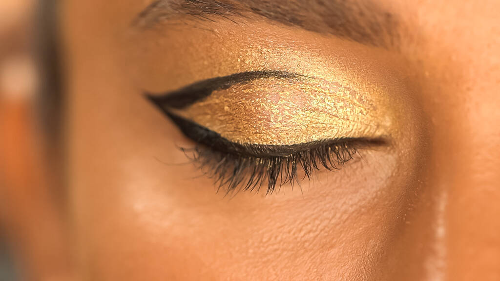 vista ritagliata di donna afro-americana con eye liner nero e ombretto dorato - Foto, immagini