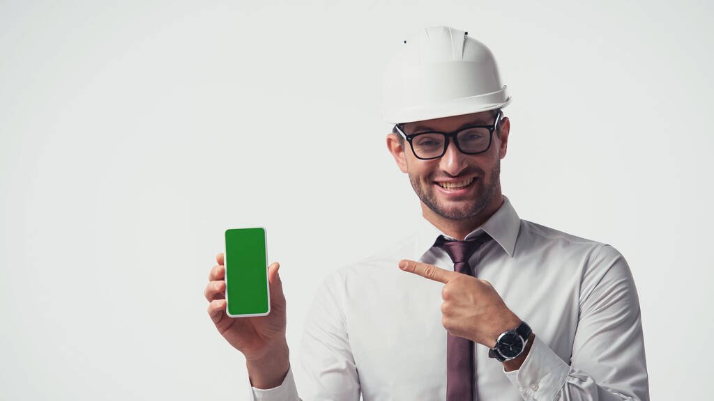 Архитектор в шлеме указывает на мобильный телефон с зеленым экраном изолирован на белом - Фото, изображение