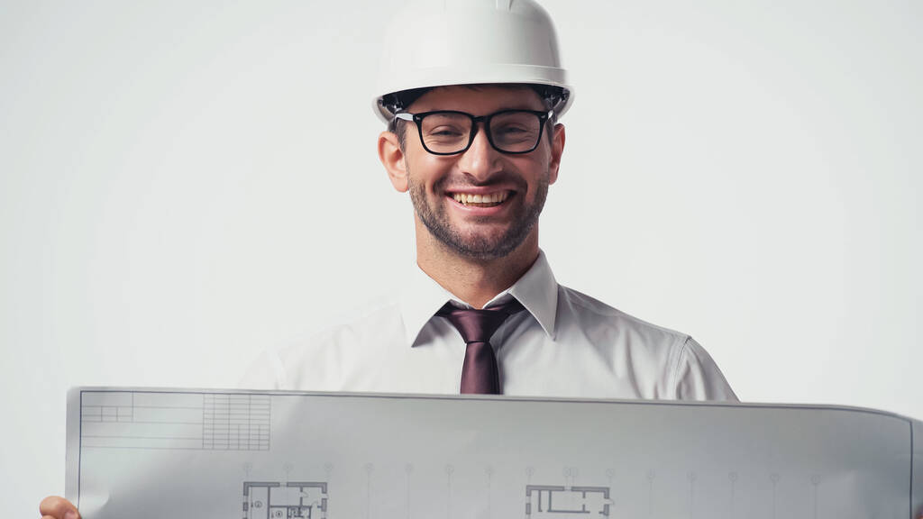 Ingeniero feliz en hardhat que sostiene el plano borroso aislado en blanco - Foto, Imagen