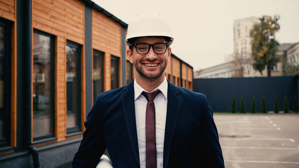 Architekt mit Brille und Helm hält Blaupause auf urbaner Straße  - Foto, Bild