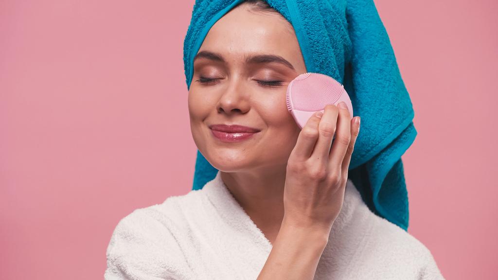femme heureuse avec les yeux fermés en utilisant une brosse nettoyante faciale en silicone isolée sur rose - Photo, image