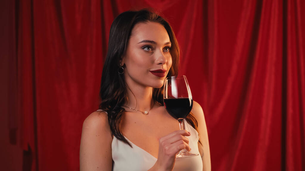 junge Frau hält Glas Wein in der Hand und lächelt rot - Foto, Bild