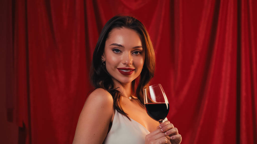 χαμογελαστή νεαρή γυναίκα κρατώντας ένα ποτήρι κρασί στο κόκκινο - Φωτογραφία, εικόνα