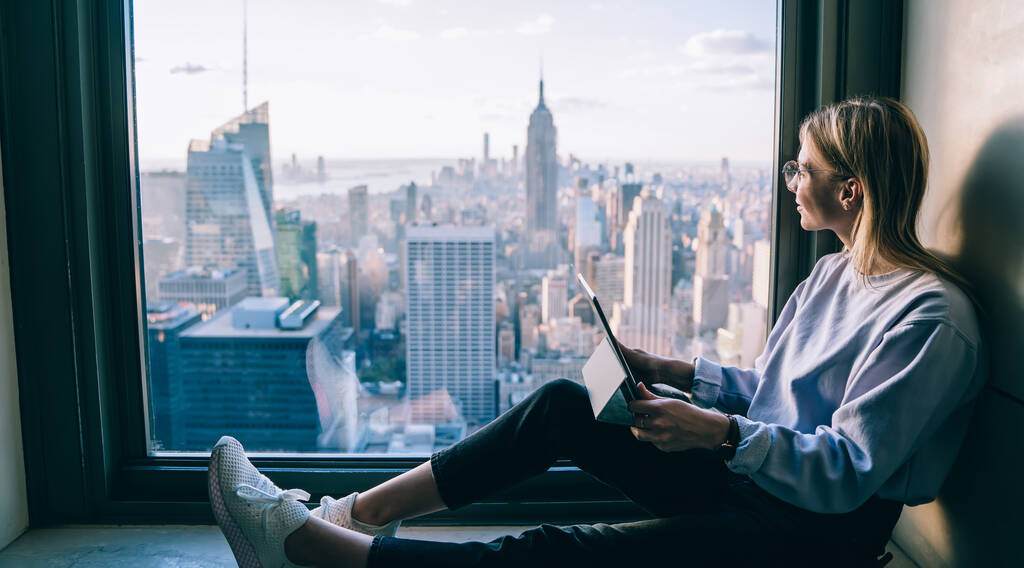 Millennial nomade digitale che guarda in vetrina panoramica durante il viaggio per visitare New York, giovane freelance con pc portatile per il lavoro a distanza sognando in alto con belvedere - Foto, immagini