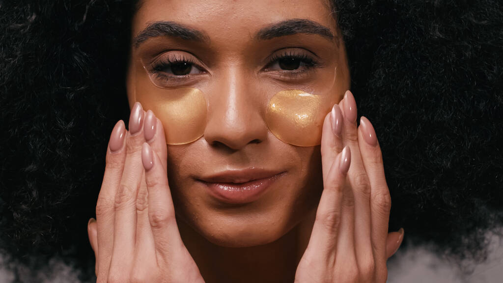 close-up van jong Afrikaans amerikaans vrouw toepassing oog patches - Foto, afbeelding