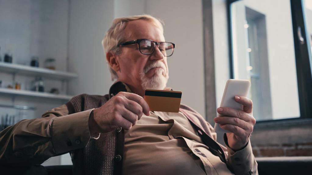 uomo anziano scontento con carta di credito in possesso di cellulare durante lo shopping online - Foto, immagini