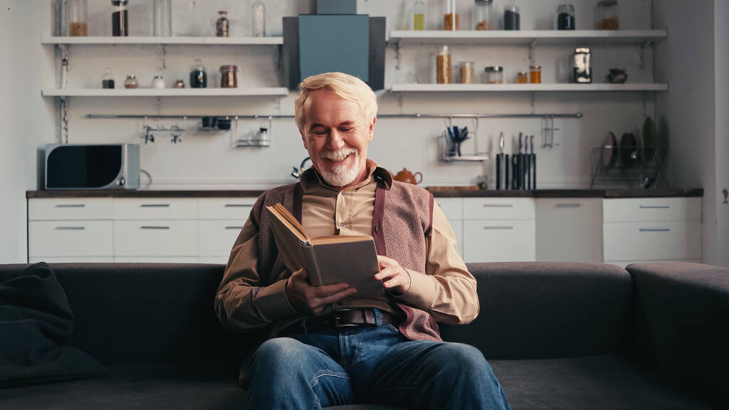 усміхнений старший чоловік читає книгу вдома
  - Фото, зображення