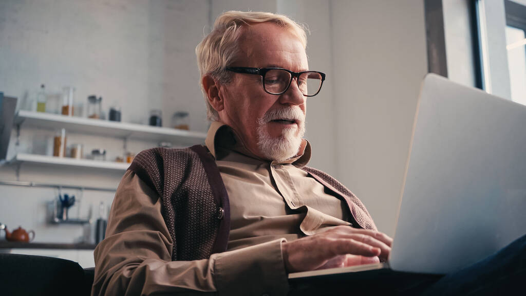 senior man in bril met laptop thuis - Foto, afbeelding