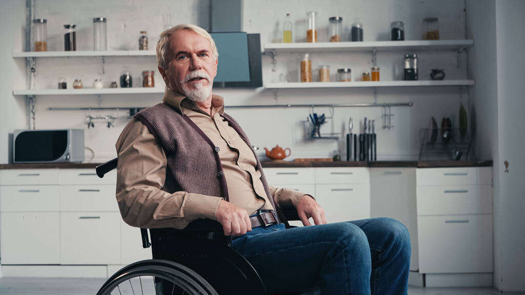 ανάπηρος συνταξιούχος που κοιτάζει την κάμερα ενώ κάθεται σε αναπηρική καρέκλα  - Φωτογραφία, εικόνα