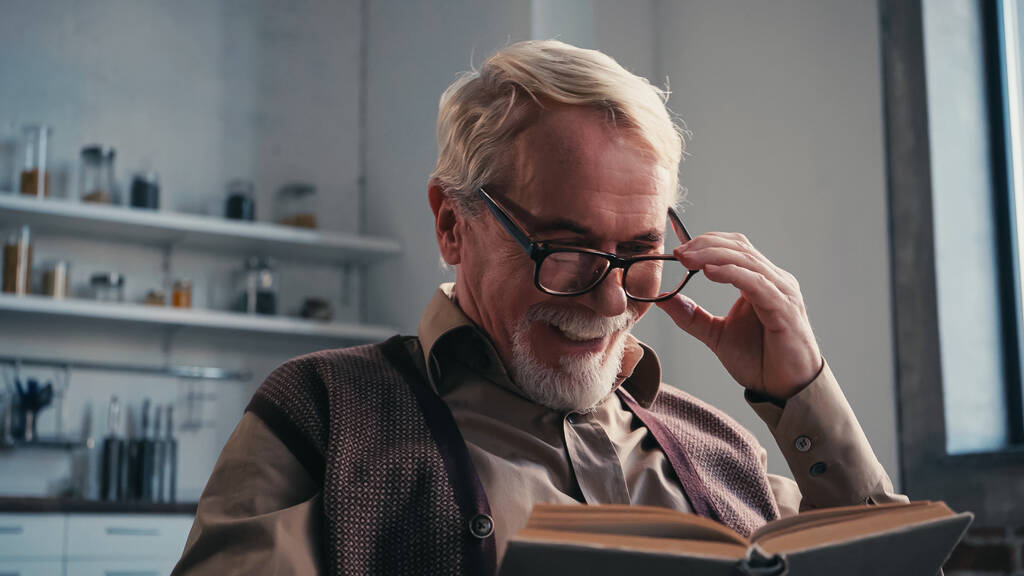 positieve senior man past bril en leesboek thuis aan  - Foto, afbeelding