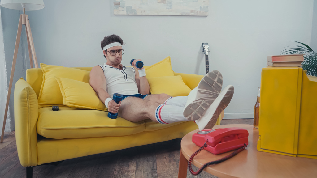 Deportista levantando pesas mientras ve la televisión en la sala de estar - Foto, Imagen