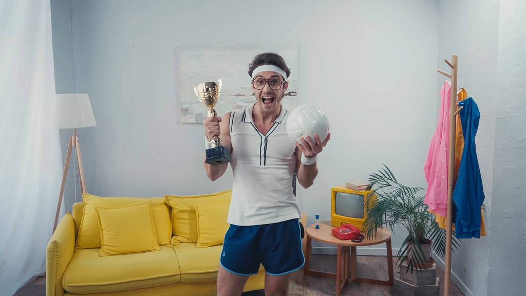 Glücklicher Mann mit Pokal und Sportball zu Hause - Foto, Bild