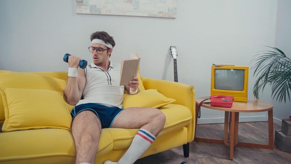 Sportember emelés súlyzó, miközben könyv a nappaliban - Fotó, kép