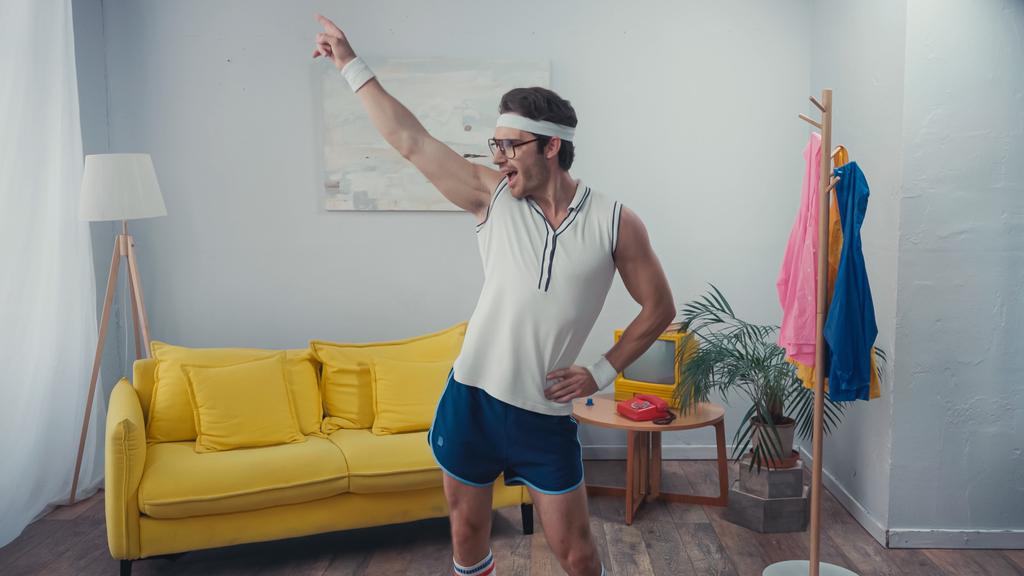 energický sportovec s rukou na hip dance v obývacím pokoji - Fotografie, Obrázek