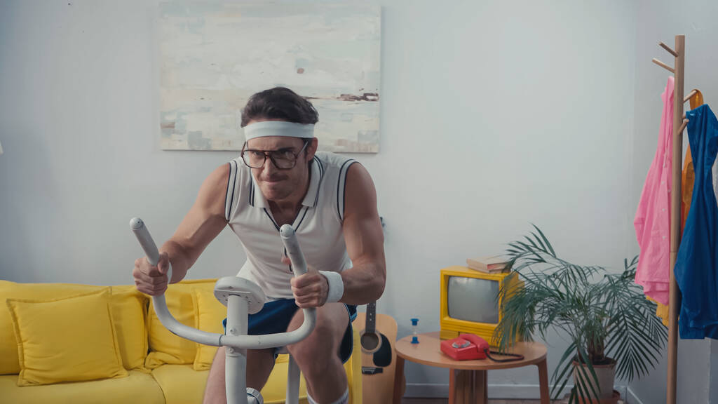 fókuszált sportoló edzés a torna kerékpár a nappaliban, retro sport koncepció - Fotó, kép
