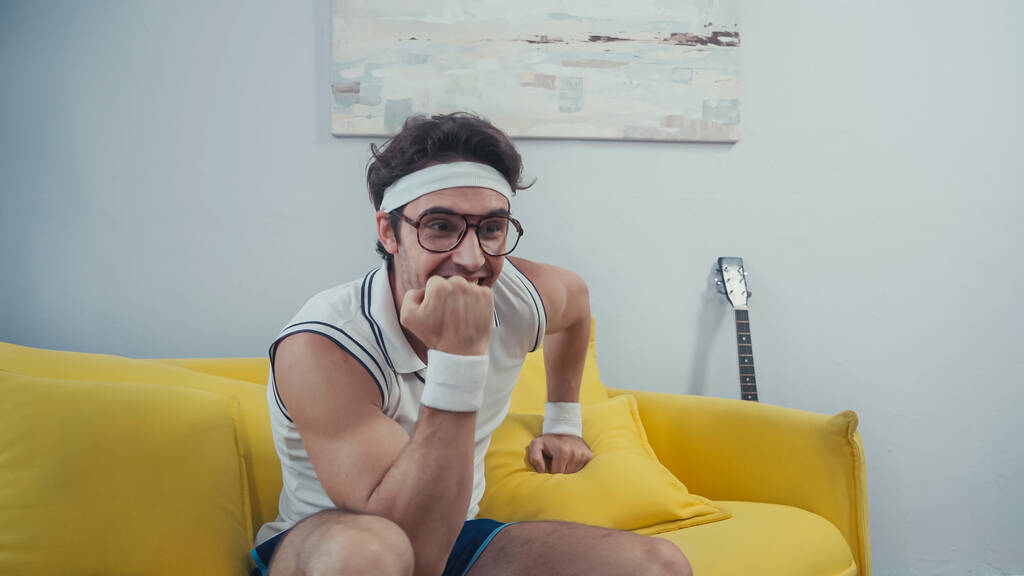 Χαρούμενος αθλητής με γυαλιά που κοιτάζει αλλού στο σαλόνι  - Φωτογραφία, εικόνα