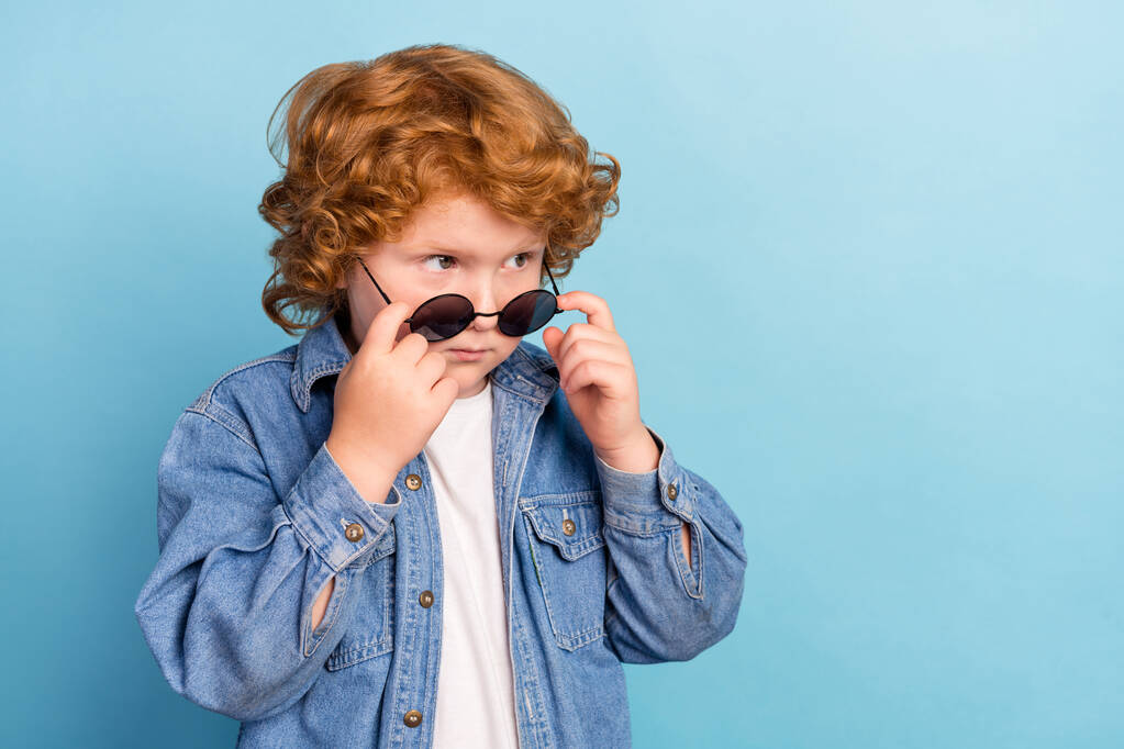 Foto Porträt lockige kleine Junge suchen leeren Raum trägt stilvolle Sonnenbrille isoliert pastellblaue Farbe Hintergrund - Foto, Bild
