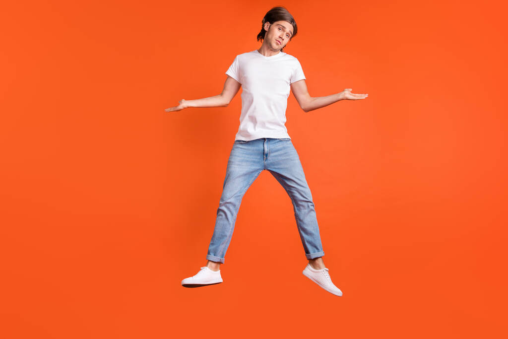 Pełne zdjęcie młodego człowieka bez wskazówki wskoczyć ramiona wzruszyć ramiona nie ma pojęcia izolowane na pomarańczowym tle koloru - Zdjęcie, obraz