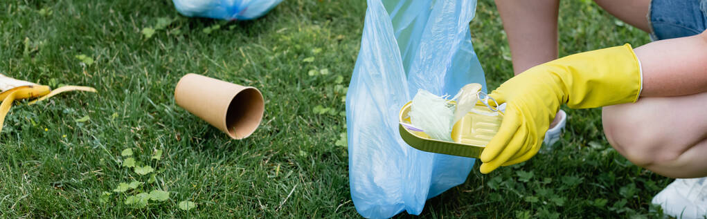 Vista recortada de la mujer sosteniendo lata y bolsa de basura al aire libre, pancarta  - Foto, imagen