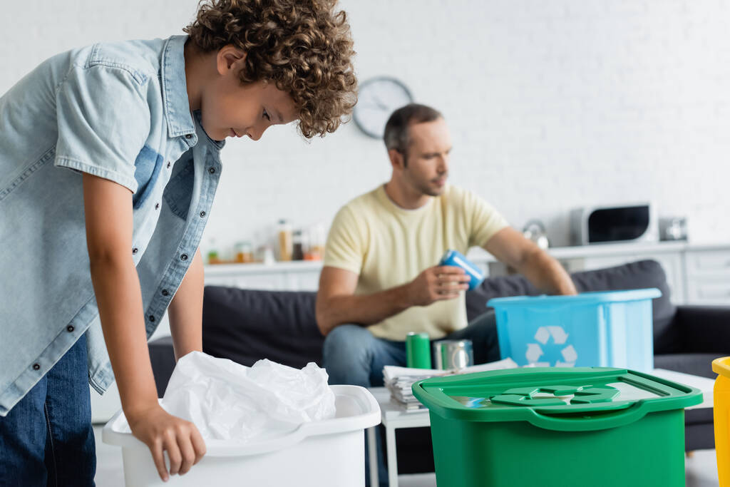 Boy standing near trash can and blurred father with garbage at home  - Photo, Image