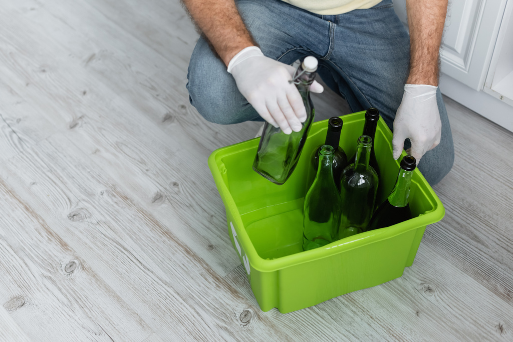 Ausgeschnittene Ansicht eines Mannes in Latexhandschuhen, der eine Schachtel mit Flaschen beim Sortieren von Müll hält  - Foto, Bild