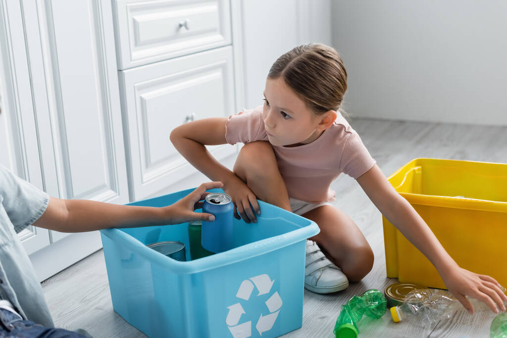 Κορίτσι κάθεται κοντά στον αδελφό, κουτιά με σκουπίδια και πινακίδα ανακύκλωσης στην κουζίνα  - Φωτογραφία, εικόνα