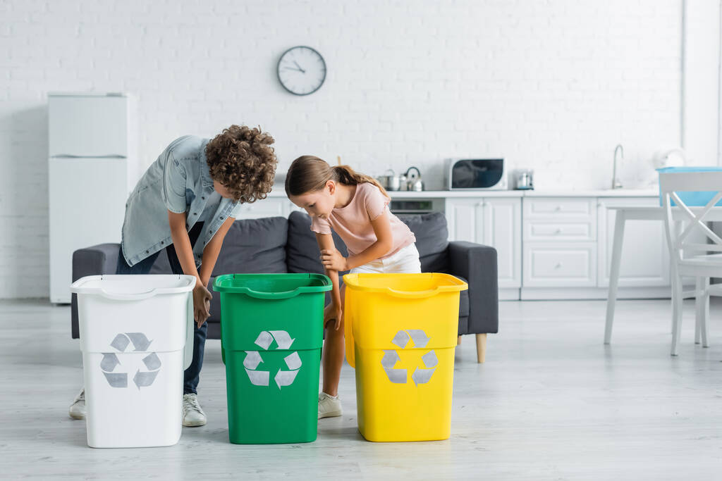 Kids looking trash cans with recycle sign in kitchen  - Photo, Image
