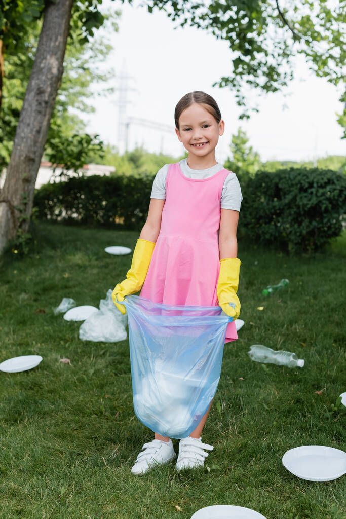 Glückliches Kind löchert Müllsack neben Müll auf Gras  - Foto, Bild