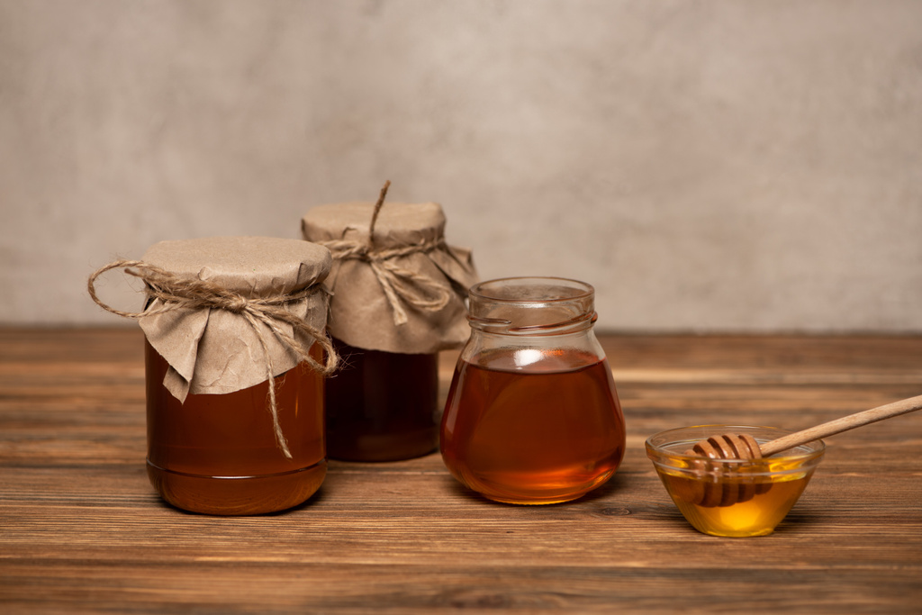 frascos com mel fresco perto da tigela com dipper na mesa de madeira e fundo de pedra cinza - Foto, Imagem