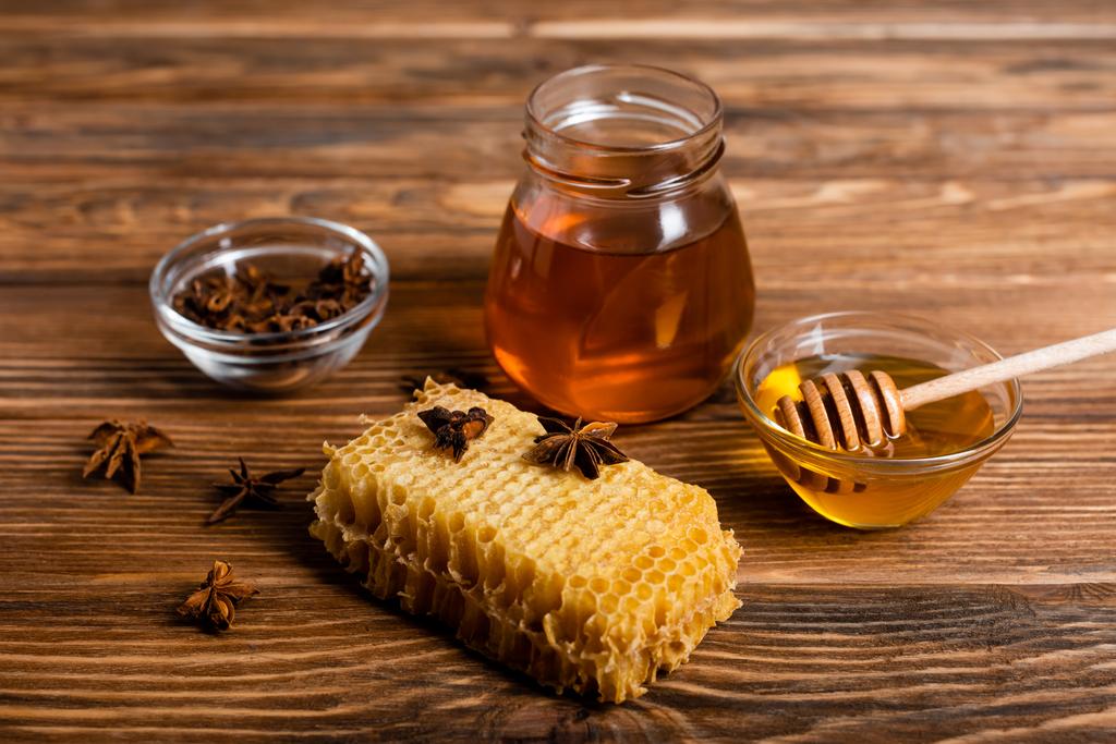 木のテーブルの上のハニカムの近くに蜂蜜とアニスの種を入れた瓶とボウル - 写真・画像