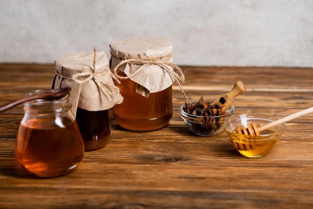 баночки та миски з медом та насінням анісу на дерев'яному столі та сірому фоні
 - Фото, зображення
