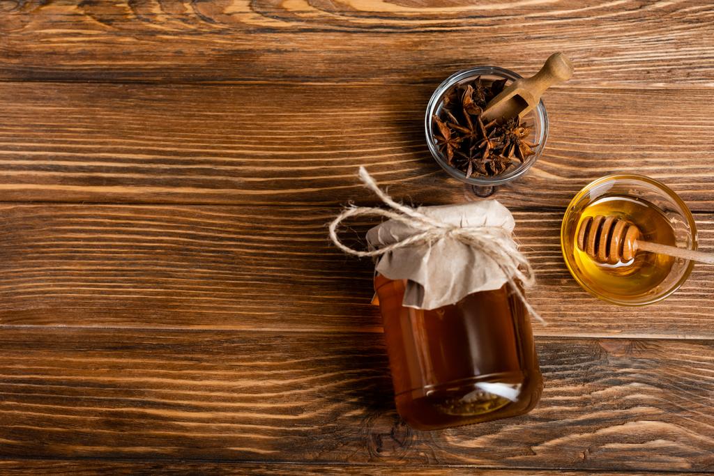 vista superior do frasco de mel coberto com papel artesanal perto de tigelas com sementes de anis, colher e mergulhador na mesa de madeira - Foto, Imagem
