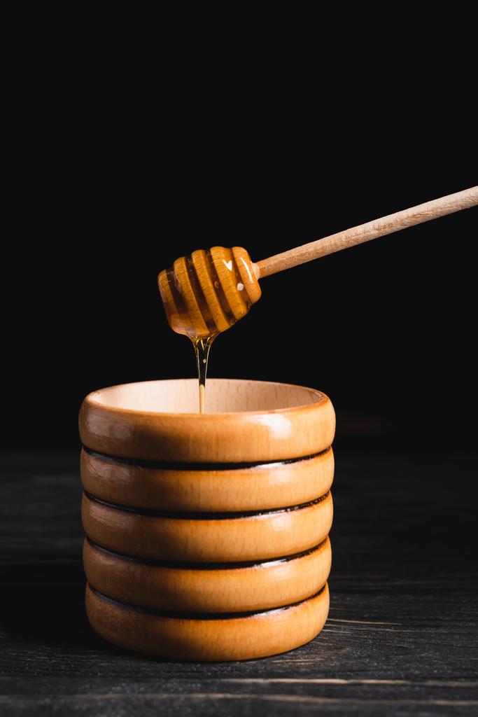 рідкий мед, що тече від занурювача в дерев'яну тару ізольовано на чорному
 - Фото, зображення