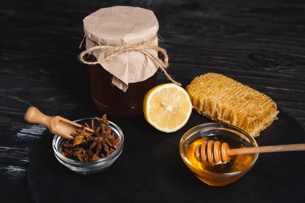 bols avec du miel et des graines d'anis près de citron frais, racine de gingembre et pot recouvert de papier artisanal sur ardoise noire - Photo, image