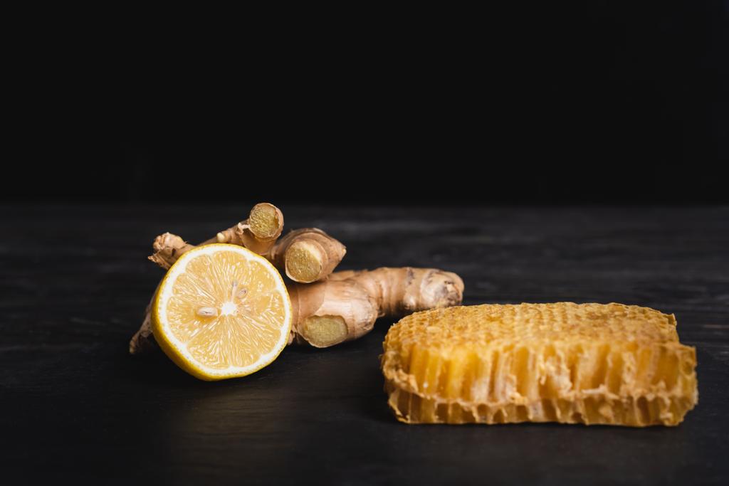 juicy lemon near ginger root and honeycomb on dark surface isolated on black - Photo, Image