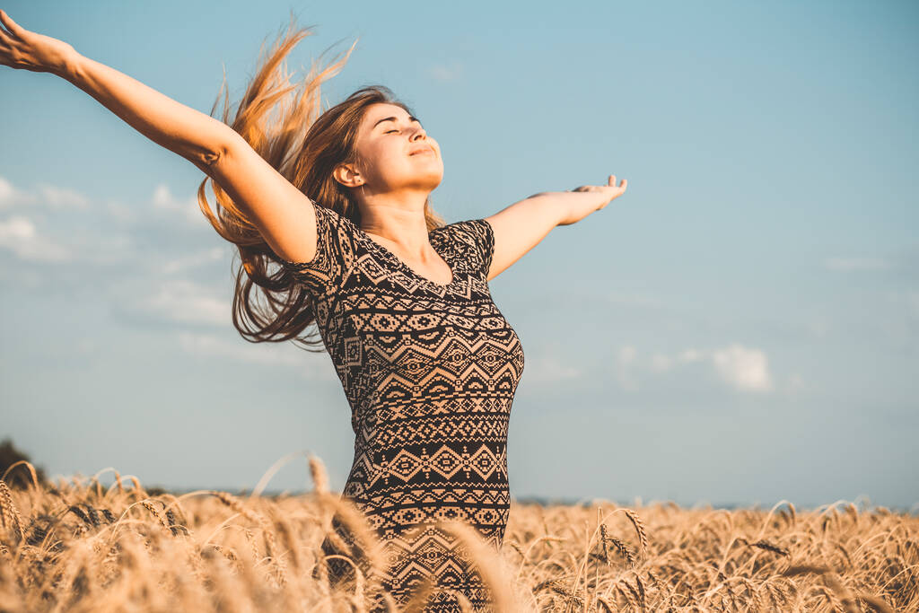 счастливая романтическая молодая женщина наслаждается природой, поднимая руки на фоне облачного неба на пшеничном поле, девушка дышит глубоко, свобода и расслабление концепции - Фото, изображение